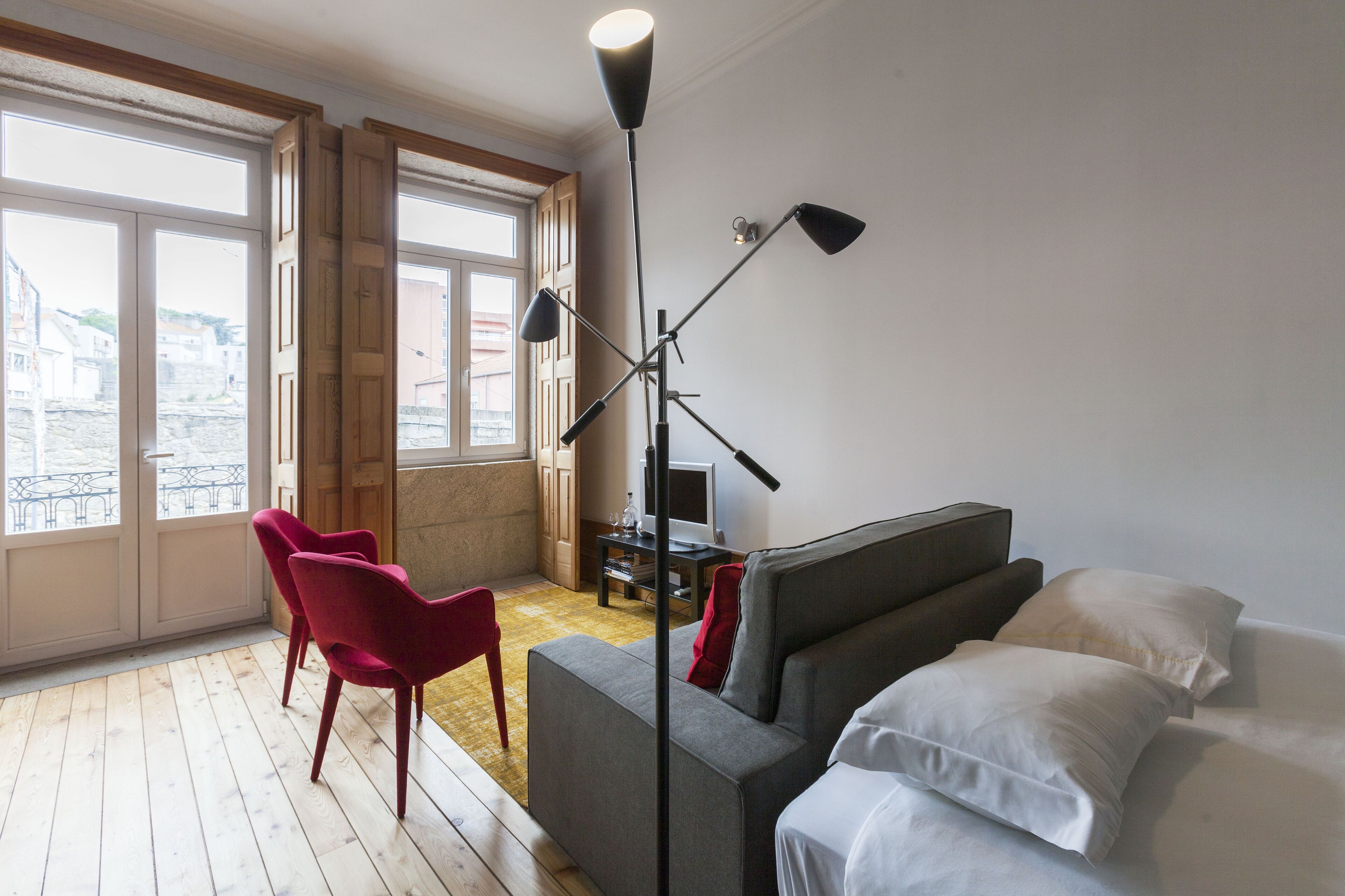 Un salon moderne avec un canapé gris, des fauteuils rouges, une lampe sur pied et un téléviseur.