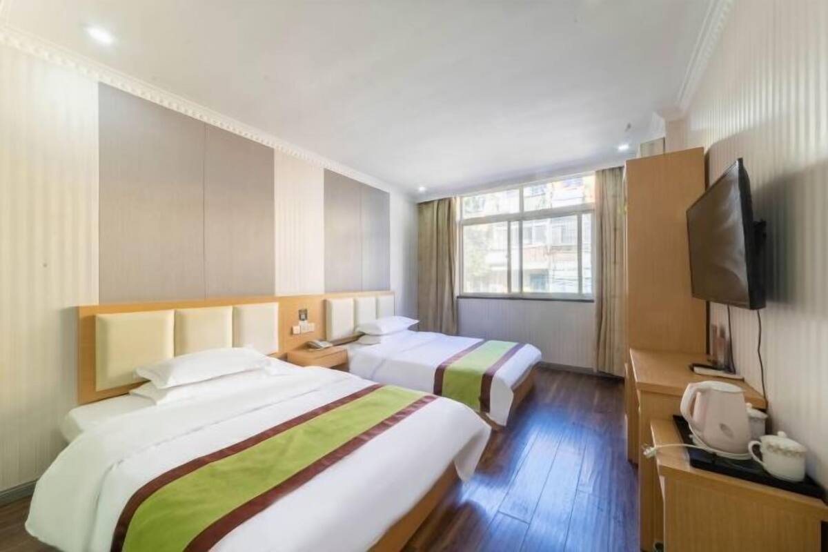 Ein Hotelzimmer mit zwei Betten, einem Fernseher, einem Schreibtisch mit Wasserkocher und einem Fenster mit Vorhängen.