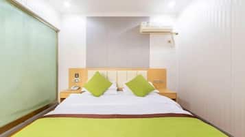 Una habitación de hotel con cama, mesita de noche, aire acondicionado de pared y ventana con persianas.