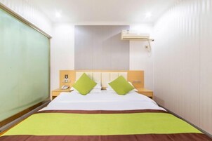 Una habitación de hotel con cama, mesita de noche, aire acondicionado de pared y ventana con persianas.