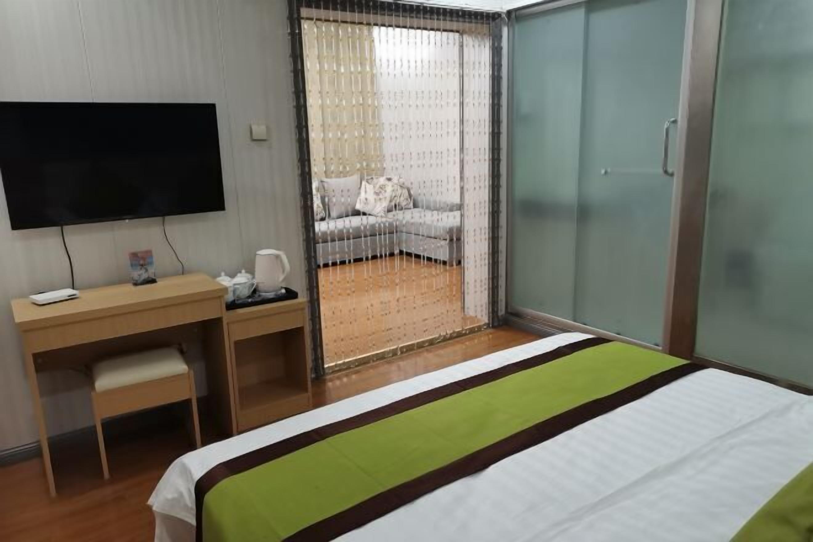 Habitación de hotel con cama, escritorio, silla, televisión y puerta corrediza que da a un balcón con sofá.