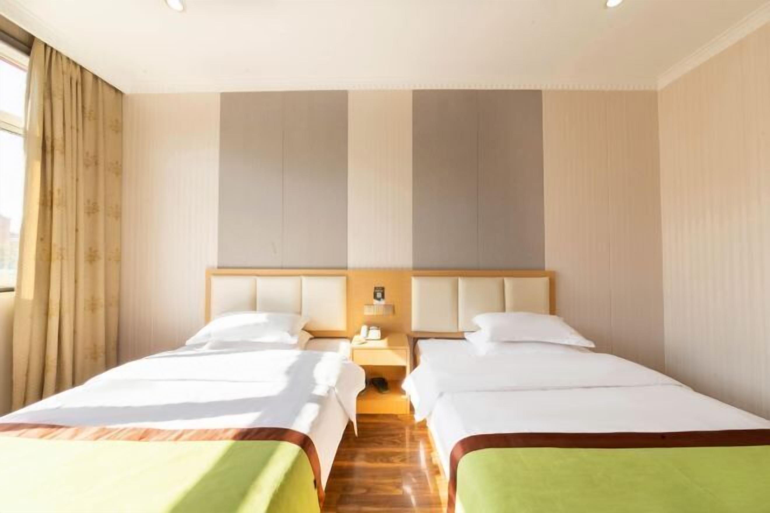 A hotel room with two beds, a wooden floor, a nightstand, and a window with curtains.