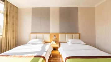 A hotel room with two beds, a wooden floor, a nightstand, and a window with curtains.