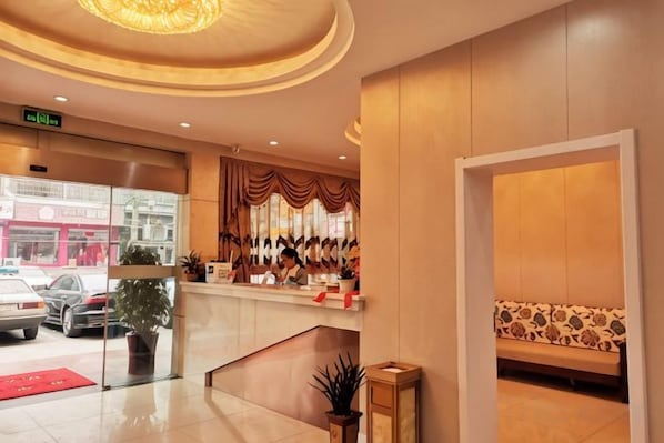 A hotel reception area with a counter, seating, and a view of the street outside.