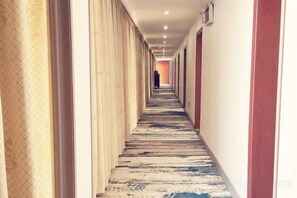 Een hotelgang met een vloerkleed met patroon, een rode muur en een deur aan het einde.