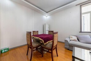 Uma área de refeições com uma mesa e quatro cadeiras, um sofá cinzento e uma janela.