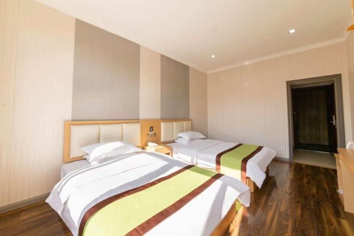 Quarto de hotel com duas camas, soalho de madeira e porta que dá para outro espaço.