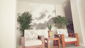 Ein Zimmer mit zwei Holzstühlen und einem kleinen Tisch, einer Wand mit einem Wandgemälde zum Thema Natur und zwei Blumentöpfen.