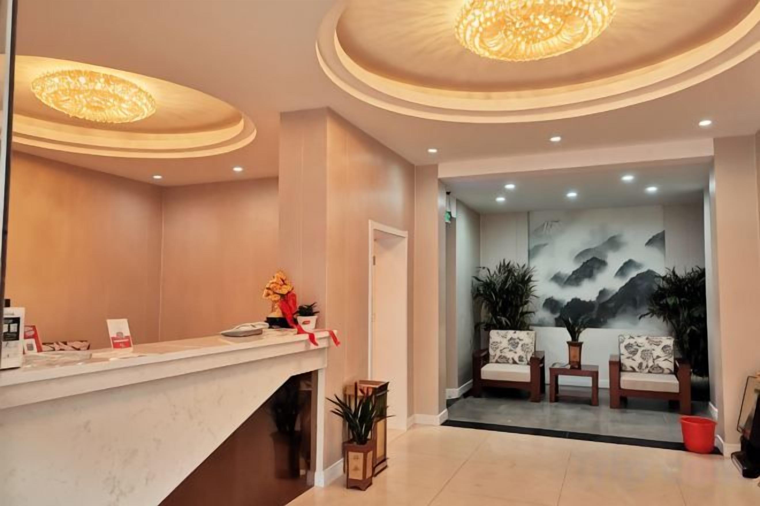 A hotel reception area with a marble counter, two seating areas with plants, and a wall with a mountain painting.