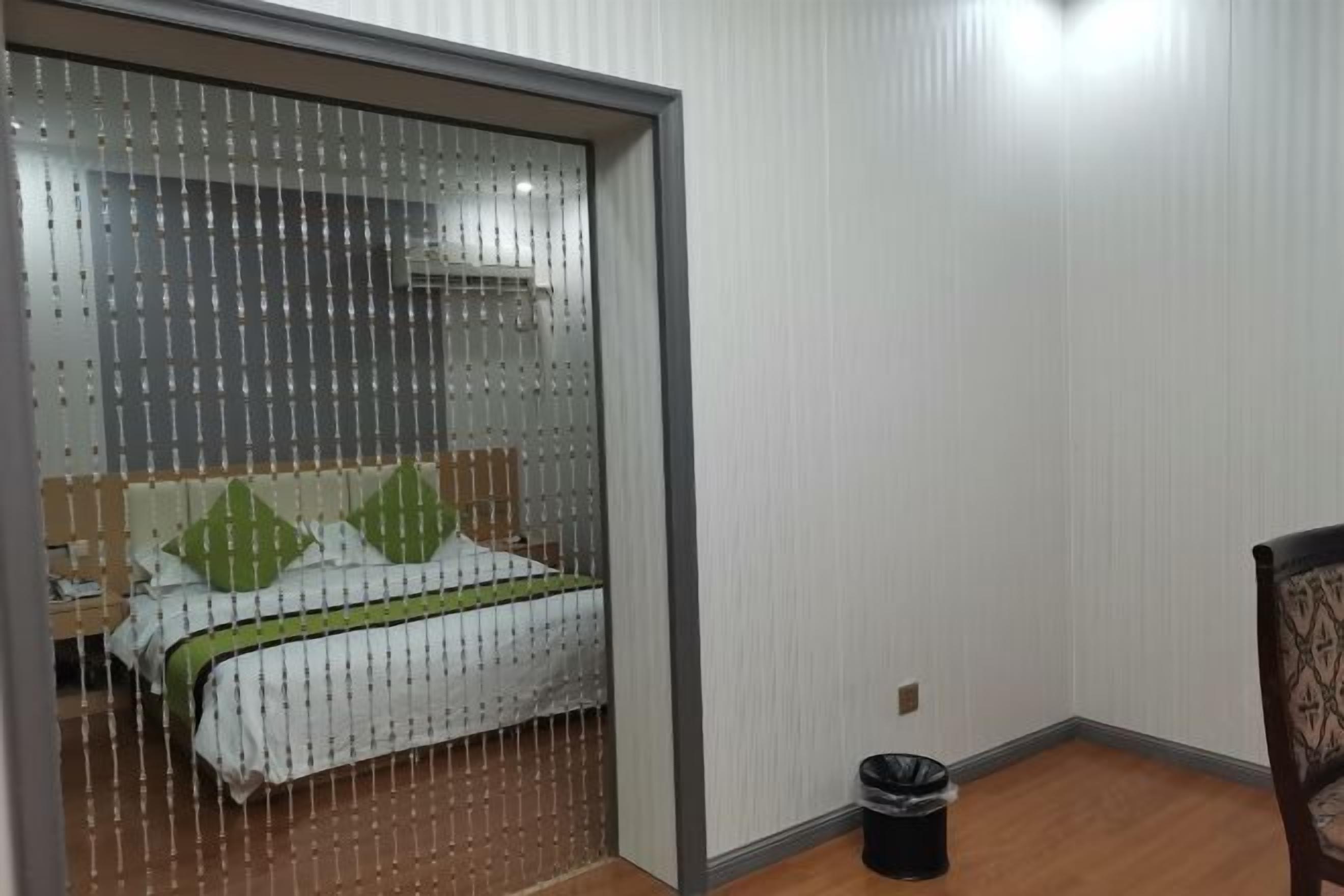 A bedroom with a bed, a nightstand, a chair, and a trash bin.