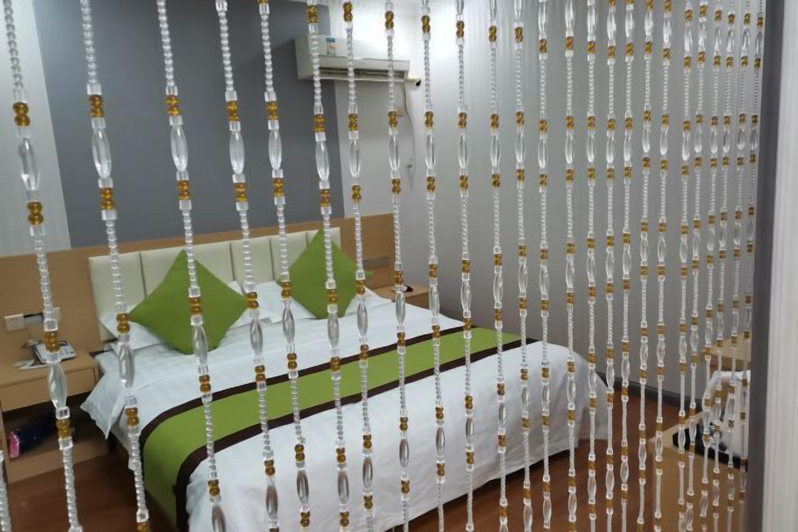 Habitación de hotel con cama, almohadas verdes, mesita de noche y aire acondicionado de pared.