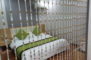 Habitación de hotel con cama, almohadas verdes, mesita de noche y aire acondicionado de pared.