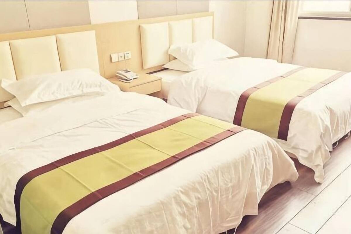 Ein Hotelzimmer mit zwei Betten, einem hölzernen Kopfende, einem Nachttisch mit Telefon und einem Fenster mit Vorhängen.