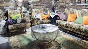 A rustic room with stone walls, floral-patterned sofas, a round coffee table, and a chandelier. - A Fonte das Bodas Pensión (Samos)