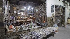 A rustic room with stone walls, a wooden table, and various decorative items. - A Fonte das Bodas Pensión (Samos)