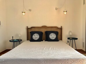 A neatly made bed with a patterned bedspread, two decorative pillows, a wooden headboard, and two bedside tables with lamps. - Villa Riccio - Charming Villa in Ericeira - Amazing Sea View (Ericeira)