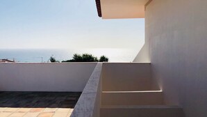 Un balcon avec vue sur la mer, un sol carrelé et un mur blanc.