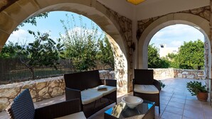 Une terrasse dotée de meubles en osier, de murs en pierre et offrant une vue sur la verdure et les bâtiments.