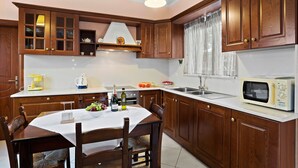 Une cuisine avec des meubles de rangement en bois, un plan de travail blanc, une table à manger avec des chaises, un four à micro-ondes et un évier.