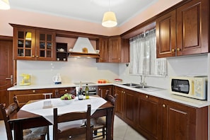 A kitchen with wooden cabinets, a white countertop, a dining table with chairs, a microwave, and a sink.