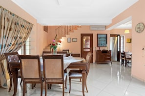 A dining area with a wooden table and chairs, a staircase, and a kitchen in the background.
