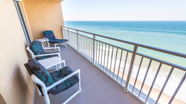 Un balcon avec deux fauteuils et une petite table, donnant sur une plage aux eaux bleu cristallin.