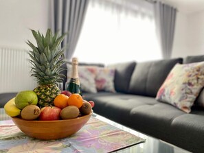 Un cuenco de fruta sobre una mesa en una sala de estar, con un sofá y cortinas al fondo.