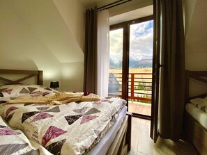 Un dormitorio con una cama grande, una mesita de noche y vistas a un balcón con montañas al fondo.
