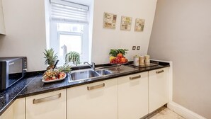 Eine Küche mit weißen Schränken, einer schwarzen Arbeitsplatte, einem Spülbecken, einer Mikrowelle und einem Fenster mit Jalousien.