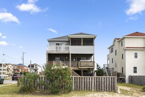 A two-story residential building with a balcony on the upper floor, a wooden fence in front, and a stop sign nearby.