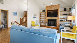 Ein geräumiges Wohnzimmer mit einem großen blauen Sofa, gelben Sesseln, einer Holz-TV-Konsole und einem Kamin.