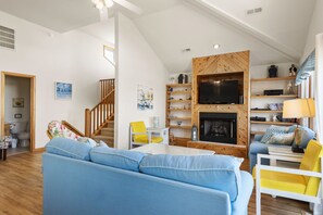 A spacious living room with a large blue sofa, yellow chairs, a wooden TV stand, and a fireplace.