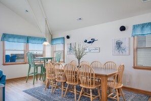 A dining area with a wooden table and chairs, a vase with branches, and artwork on the walls.