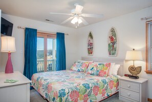A bedroom with a bed, a nightstand, a ceiling fan, and a window with curtains.