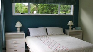 Une chambre à coucher avec un lit, deux tables de chevet, une fenêtre donnant sur un paysage verdoyant et un lambrequin à rayures.