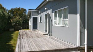 Une maison moderne à deux étages, dotée d’une terrasse en bois, de grandes fenêtres et d’une façade grise.