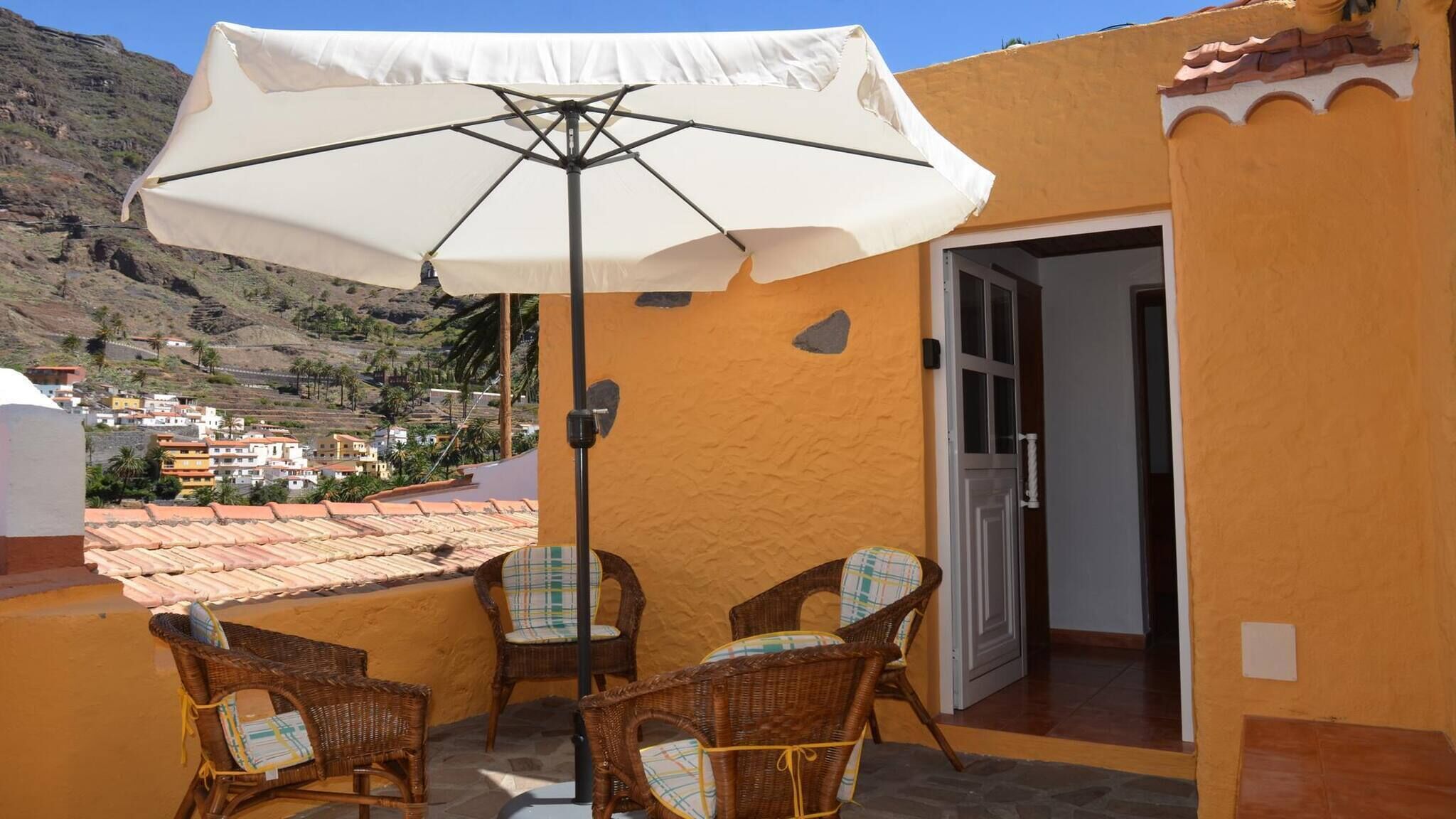 A patio with wicker chairs and a large umbrella, overlooking a hillside town.