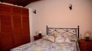 Ein Schlafzimmer mit einem Bett, einem Holzschrank, zwei Wandleuchten und einem Nachttisch mit Lampe.