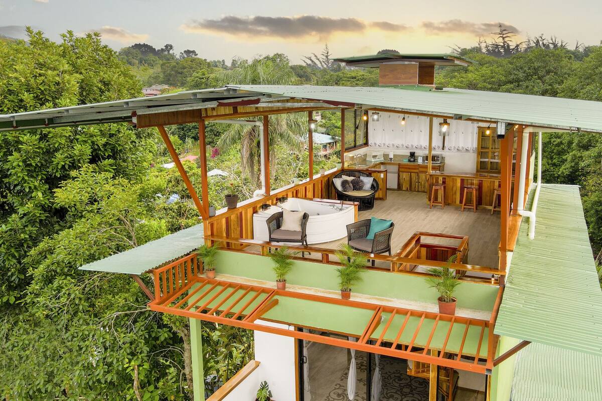 A two-story wooden house with a balcony, a hot tub, and a kitchen area.