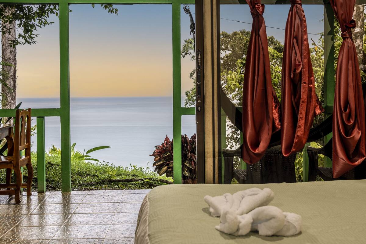 A room with a bed, a view of the sea, and a green railing.