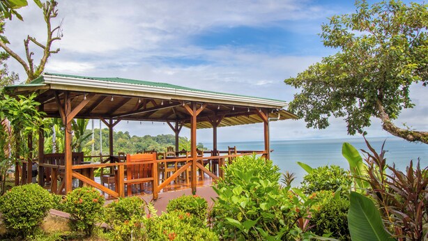 A wooden deck with tables and chairs overlooking a body of water. - Cotingas Ocean View (Drake Bay)
