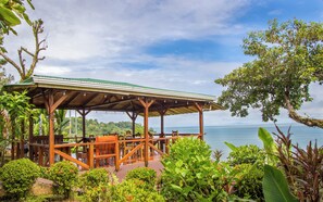 A wooden deck with tables and chairs overlooking a body of water. - Cotingas Ocean View (Drake Bay)