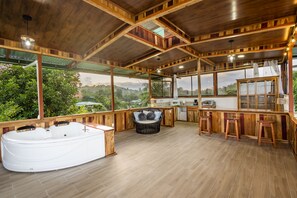 A spacious outdoor area with a hot tub, wooden deck, and a bar area with stools.