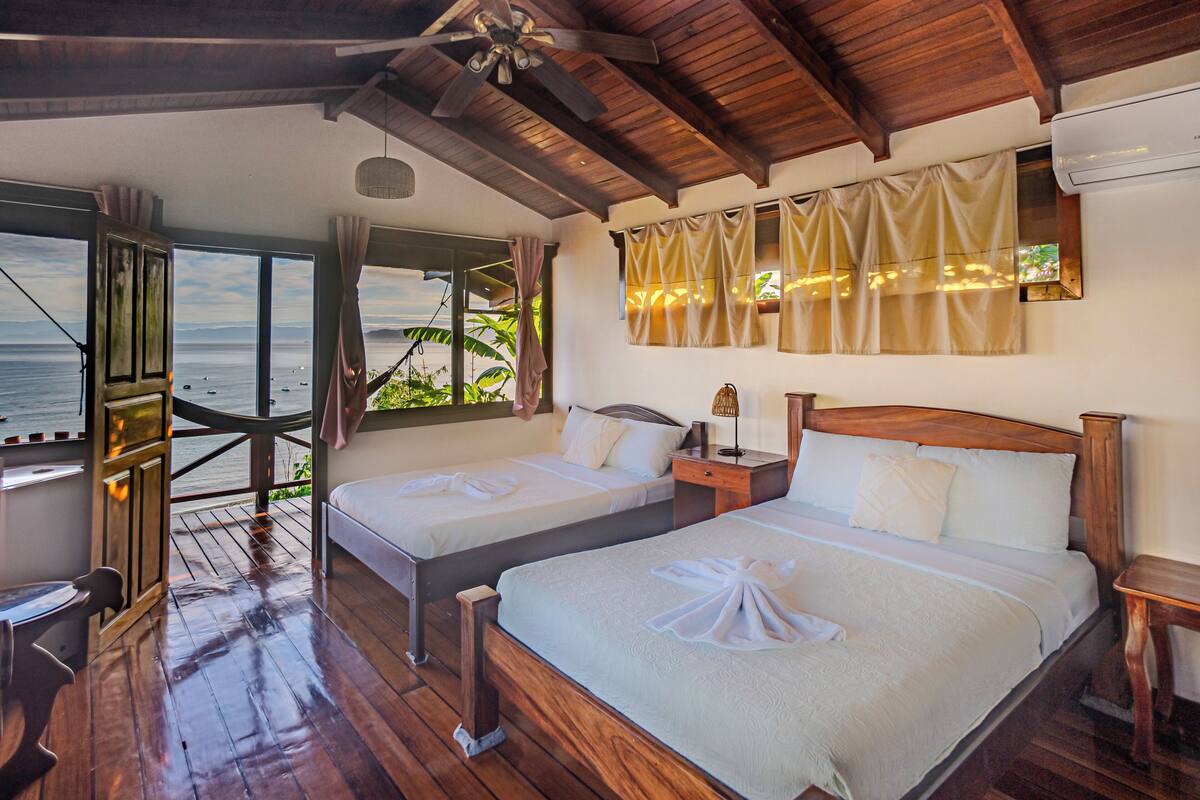 A wooden deck with two beds, a ceiling fan, and a view of the ocean.
