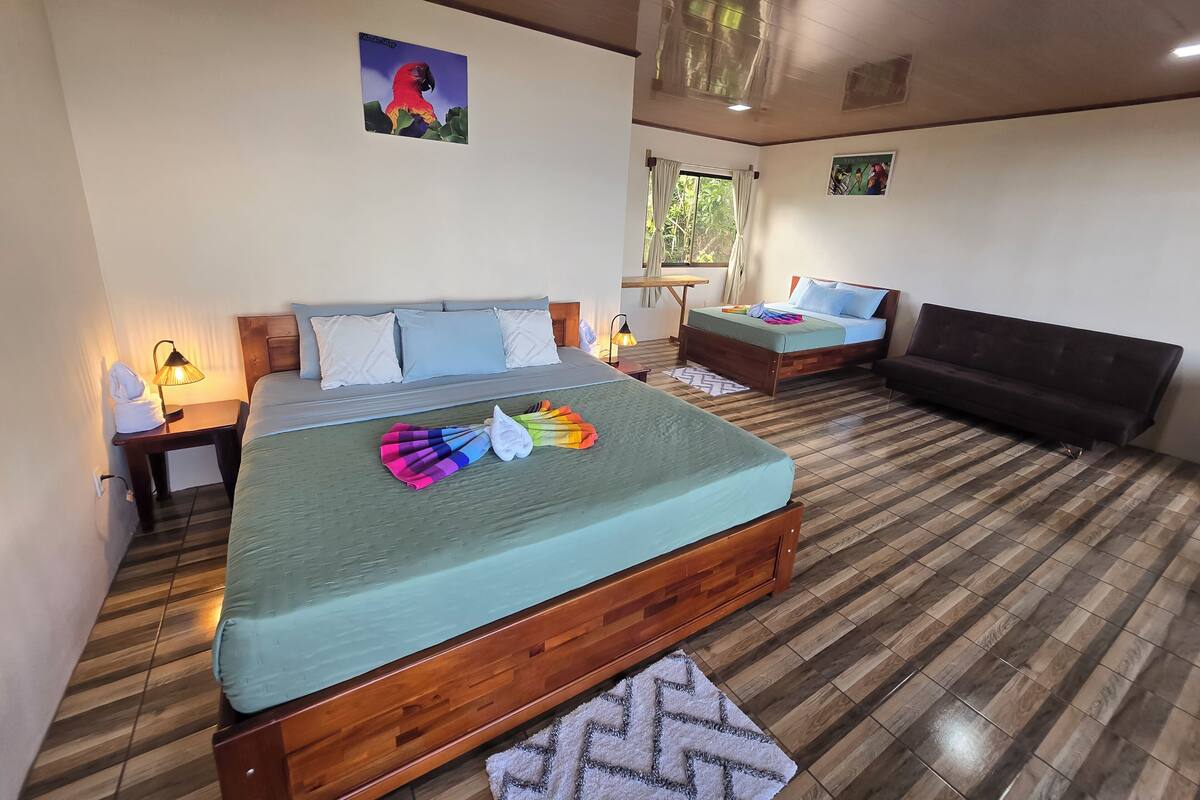 A bedroom with a wooden bed, a sofa, a nightstand, a lamp, and a window with curtains.
