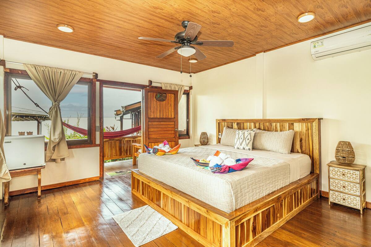 A wooden-framed bed with a view of the outdoors, a ceiling fan, and a small bedside table with a decorative item.