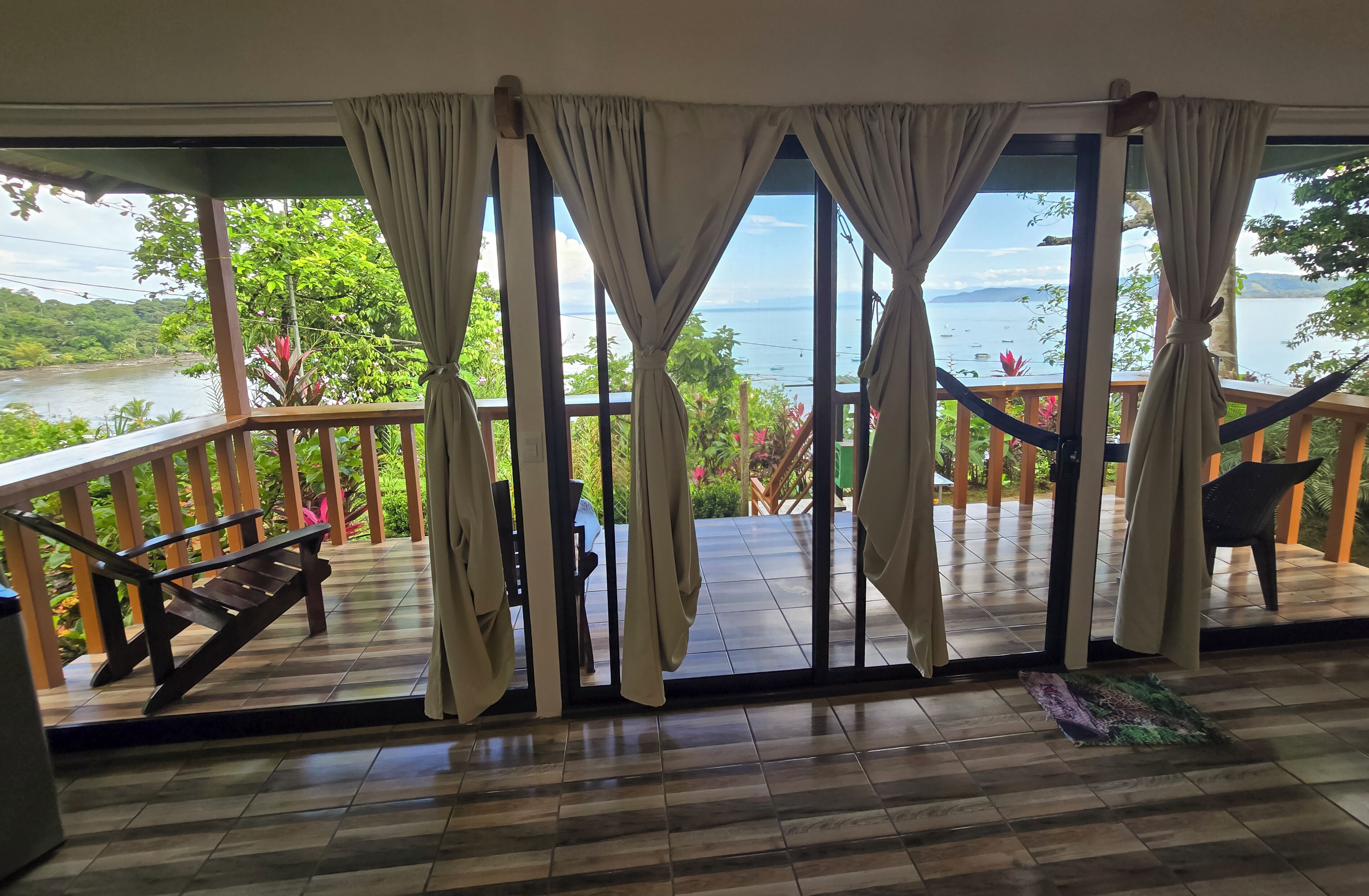 Quarto com vista para um rio e montanhas, escada de madeira e varanda com uma cadeira.