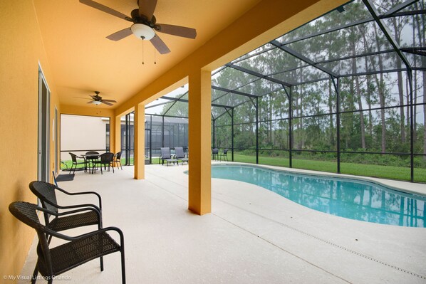 Relax by the pool in a serene outdoor space with a seating area, glass enclosure, and ceiling fan.