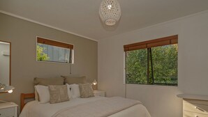 Une chambre à coucher avec un grand lit, des tables de chevet, une commode, une coiffeuse et une fenêtre donnant sur un paysage verdoyant.