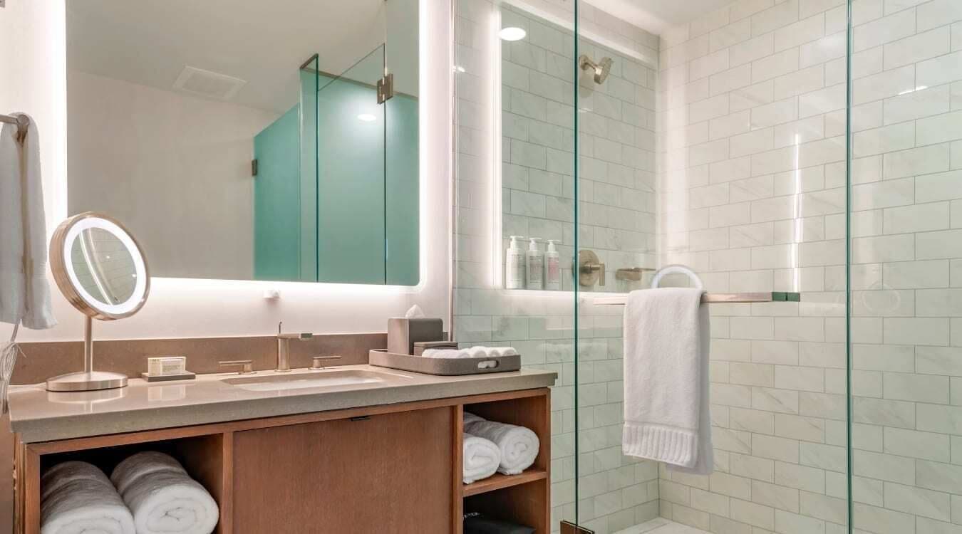 A modern bathroom with a glass shower enclosure, a vanity with a mirror, and neatly rolled towels.
